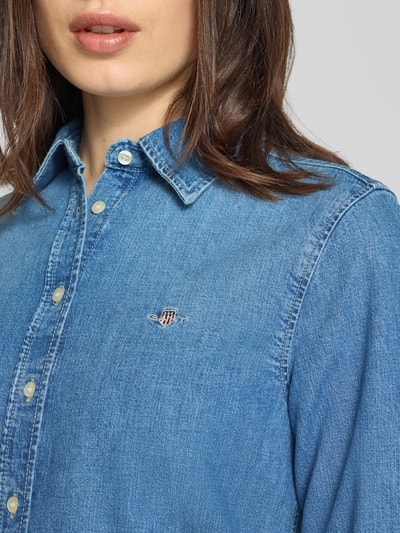 Vrouwenmodel draagt Jeansbluse met Logo-Stitching en Sportmanschetten van Gant in helderblauw denim, knoopsluiting, kentkraag, afgeronde zoom, regular fit, pure katoen, detailopname bovenlichaam.