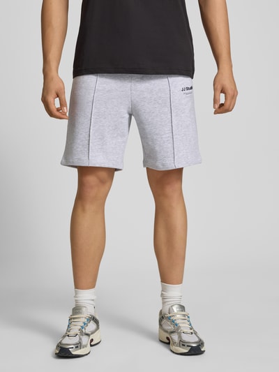 Männermodel trägt Sweatshorts mit Logo Modell 'KANE' von Jack & Jones aus Baumwoll-Mix, Relaxed-Fit, grau; Ganzkörperansicht von vorne.
