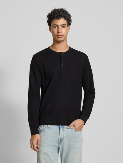Männermodel trägt Regular Fit Longsleeve in Strick-Optik Modell 'Niagara' von JACK & JONES in Schwarz aus Baumwoll-Mix, Henley-Ausschnitt, Ganzkörperansicht von vorne.