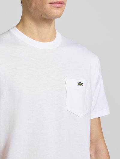Männermodel trägt Regular Fit T-Shirt aus reiner Baumwolle von Lacoste, weiß, unifarben, mit Logo-Stitching, Rundhals, Nahaufnahme Oberkörper.