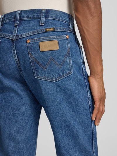 Męski model nosi Cowboy Cut Jeans im 5-Pocket-Design od Wrangler, czysty bawełniany dżins, niebieski, prosty krój, detal tylnej kieszeni, szerokość w rozmiarze 32/32: 44 cm, długość nogawki: 81 cm, zapięcie na guzik i zamek, widok z tyłu detalowy.