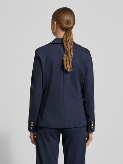 Vrouwenmodel draagt Slim Fit Blazer uit viscosemix model 'Ritmo' van Marella in donkerblauw, getailleerde pasvorm, elastische stof, reverskraag, dubbele knoopsluiting, paspelzakken, ruglengte 60 cm, borstwijdte 42 cm, mouwlengte 58 cm, volledige lichaamsopname achteraan.