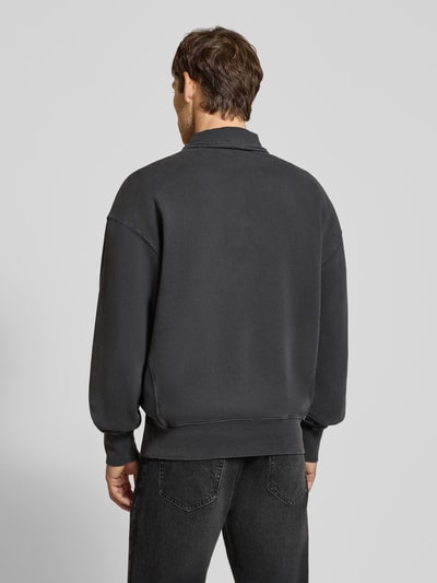 Männermodel trägt Relaxed Fit Troyer aus reiner Baumwolle Modell 'ICONIC' von ARMEDANGELS in Dunkelgrau, strukturierte Oberfläche, Ganzkörperansicht Rückansicht.