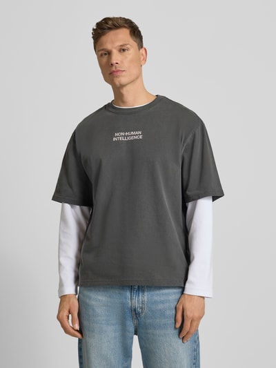 Männermodel trägt ein graues T-Shirt mit Rundhalsausschnitt Modell 'Gary' von Wood Wood aus reiner Baumwolle, Ganzkörperansicht von vorne.