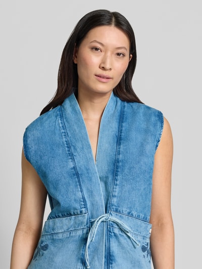 Modelka kobieca nosi Jeansweste mit Schnürung Modell 'GILLIAN' od Mustang, czysta bawełna, krój regular fit, jasnoniebieski denim, tekstura gładka, kieszenie wpuszczane, długość pleców w rozmiarze S: 68 cm, szerokość w rozmiarze S: 45 cm, zbliżenie na górną część ciała z przodu.