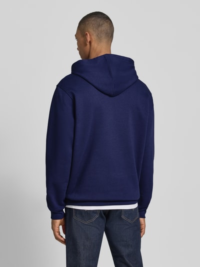Männermodel trägt Oversized Hoodie mit Logo-Stitching von GAP in Dunkelblau, Baumwoll-Mix, Oversized-Fit, Rückenansicht Ganzkörperansicht. Rückenlänge bei Größe L: 72 cm, Kapuze mit Tunnelzug, Känguru-Tasche, elastische Abschlüsse, Ärmellänge bei Größe L: 65 cm.