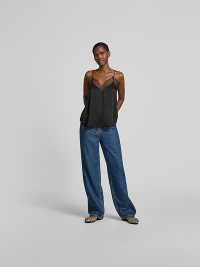 Frauenmodel trägt Top mit Spitzenbesatz von Iro in Schwarz, Relaxed-Fit, V-Ausschnitt, Spaghetti-Träger, semitransparente Partien, kombiniert mit blauer Jeans, Rückenlänge bei Größe 36: 46 cm, Ganzkörperansicht von vorne.