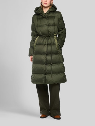 Frauenmodel trägt Steppmantel mit Bindegürtel von Marc Cain in Olivgrün, mit Kapuze und verdecktem Reißverschluss, Ganzkörperansicht von vorne. Regular Fit, Eingrifftaschen, Rückenlänge 107 cm, Schulterbreite 43 cm, Brustweite 58 cm, Ärmellänge 63 cm.