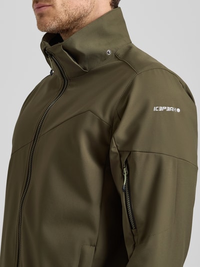 Męski model nosi Regular Fit Jacke mit Kapuze Modell 'BARMSTEDT' od Icepeak w oliwkowym kolorze, tekstura gładka, logo na ramieniu, widoczna kieszeń na rękawie z zamkiem, krój regular fit, stójka, kieszenie boczne, zamek błyskawiczny, nadruk z logo, długość tyłu w rozmiarze 50: 78 cm, szerokość ramion w rozmiarze 50: 43 cm, szerokość klatki piersiowej w rozmiarze 50: 54 cm, długość rękawa w rozmiarze 50: 71 cm, zbliżenie na górną część tułowia z przodu