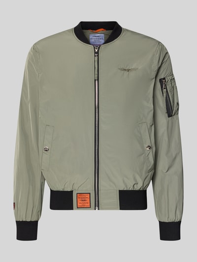 Produktfoto, Bomberjacke mit Label-Patch und Eingrifftaschen von Original Bombers, olivgrün, Gerader-Schnitt, Reißverschluss, Reißverschlusstasche am Ärmel, gerippte Abschlüsse, Detailaufnahmen zeigen Textur des leichten, glatten Stoffes, Größe M: Rückenlänge 67 cm, Schulterbreite 43 cm, Brustweite 53 cm, Ärmellänge 68 cm.