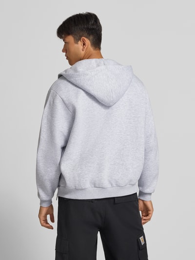Männermodel trägt Sweatjacke mit Label-Stitching und Känguru-Tasche von Karl Kani in Hellgrau, lockerer Schnitt, Rückenansicht, Ganzkörperansicht. Baumwoll-Mix, Regular Fit, Kapuze, Reißverschluss, Känguru-Tasche, Rückenlänge 68 cm, Ärmellänge 66 cm.