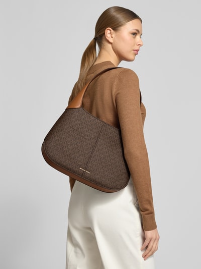 Frauenmodel trägt Shoulder Bag mit Allover-Logo-Print Modell 'Alice' von MICHAEL Michael Kors in Braun, Detailaufnahme Rückansicht. Schulterriemen, Reißverschlussfach innen, Maße 31x24x7 cm, Länge Riemen 65 cm.