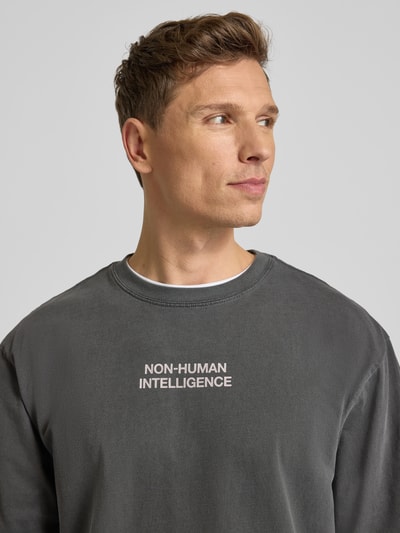 Männermodel trägt T-Shirt mit Rundhalsausschnitt Modell 'Gary' von Wood Wood in Dunkelgrau, reine Baumwolle, Relaxed Fit, Nahaufnahme Oberkörper.