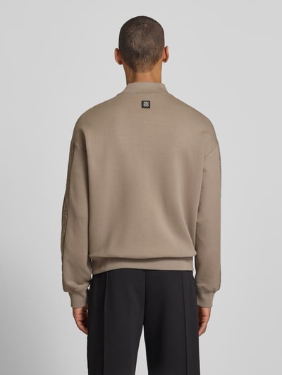 Männermodel trägt Oversized Sweatjacke aus Baumwoll-Mix Modell 'DROMZIP' von HUGO in Beige mit College-Kragen, Ganzkörperansicht Rückansicht.