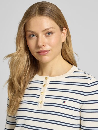 Vrouwenmodel draagt Regular Fit Langarmshirt uit katoenmix van Tommy Hilfiger, all-over gestreept motief, logo-stitching, henley-hals, knitwearstructuur, kleur licht crème met donkerblauwe strepen, detailopname bovenlichaam