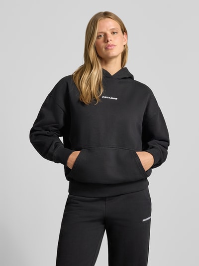 Frauenmodel trägt Relaxed Fit Hoodie aus Baumwoll-Mix Modell 'Clarita' von PEGADOR, schwarz, Logo-Stickerei, Kängurutasche, Ganzkörperansicht von vorne.