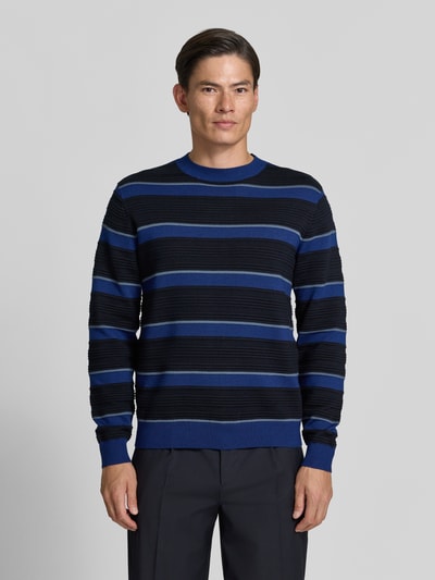 Männermodel trägt Strickpullover mit Struktur-Muster von Armani Exchange in Blau und Schwarz mit Rundhalsausschnitt, Nahaufnahme Oberkörper. Reine Baumwolle, lockerer Schnitt, gerippte Abschlüsse.