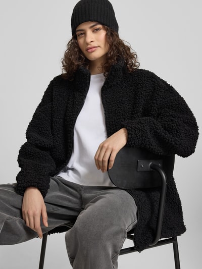Frauenmodel trägt schwarze Jacke aus Teddyfell mit Stehkragen von Karo Kauer, oversized, Reißverschluss, strukturierte Optik, Nahaufnahme Oberkörper.