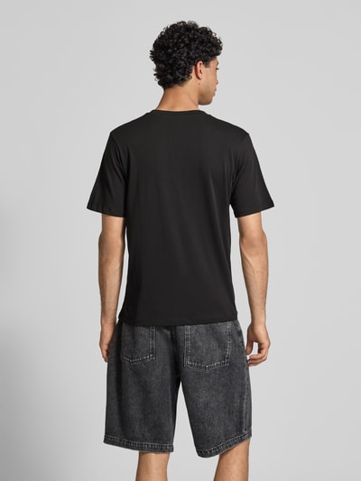 Męski model nosi t-shirt z nadrukiem z napisem model 'RHYERES' od Jack & Jones z woskowanej bawełny, krój regular fit, okrągły dekolt, długość tyłu w rozmiarze m: 67 cm, widok całej sylwetki od tyłu.