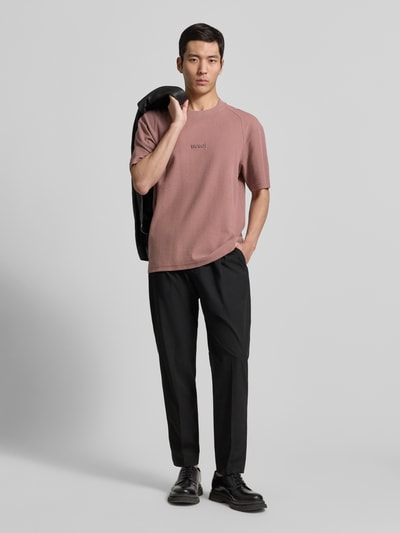 Männermodel trägt Regular Fit T-Shirt aus reiner Baumwolle Modell 'DAFFL' von HUGO in Rosé, strukturierte Jacquard-Optik, unifarben, Rundhalsausschnitt, kurze Ärmel, Label-Applikation, klassische Hose und schwarze Schuhe; Ganzkörperansicht von vorne.