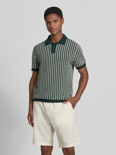 Męski model nosi Regular Fit Poloshirt in Strick-Optik od MCNEAL z bawełny, krój regular fit, imitacja dzianiny, kołnierzyk polo, krótki rękaw, długość tyłu 71 cm, długość rękawów 24 cm, przód, kolor zielony z kremowymi paskami, tekstura prążkowana; całkowite ujęcie od przodu.