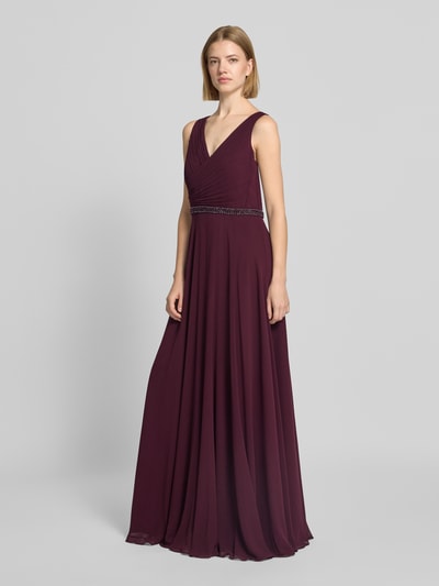 Frauenmodel trägt Fit and Flare Abendkleid mit Perlenstickerei von Vera Mont in dunklem Bordeaux mit fließendem Stoff, Ganzkörperansicht von vorne.
