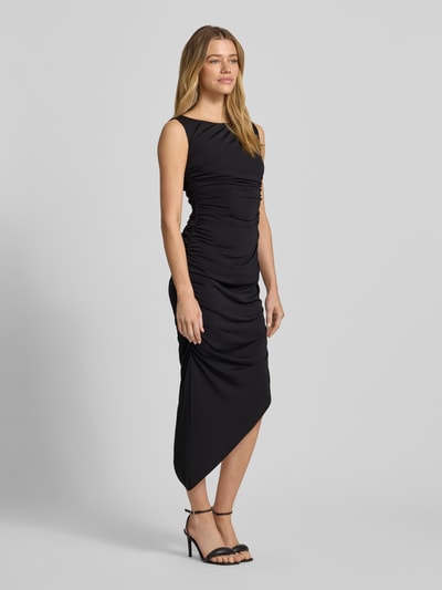 Frauenmodel trägt Cocktailkleid in asymmetrischer Form von Jake*s Cocktail, schwarzer Material-Mix mit Drapierungen, Ganzkörperansicht von vorne.