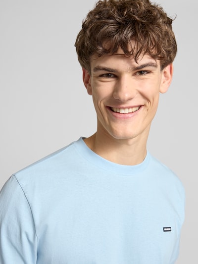 Männermodel trägt Basic T-Shirt mit kleinem Logo-Patch auf der Brust von REVIEW in Hellblau, reine Baumwolle, Nahaufnahme Oberkörper.