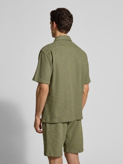 Männermodel trägt Regular Fit Freizeithemd mit Strukturmuster von MCNEAL in Olivgrün, Elastischer-Material-Mix, Kurzärmelig, Reverskragen, Ganzkörperansicht Rückansicht