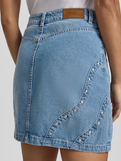 Frauenmodel trägt Jeansrock mit Nieten Modell 'CLIO' von YAS aus Reine Baumwolle, hellblau mit Teilungsnähte, Minirock, Ganzkörperansicht Rückansicht.