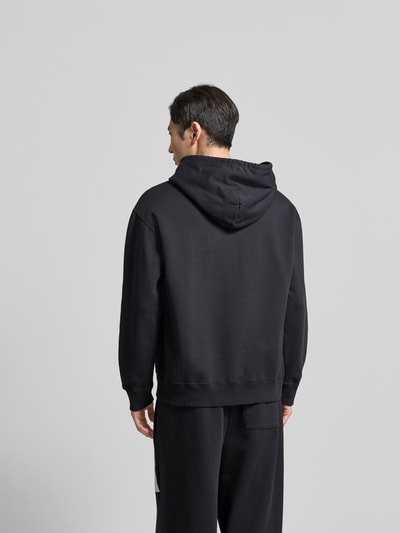 Männermodel trägt schwarzen Hoodie mit Label-Stitching von MM6 Maison Margiela, reine Baumwolle, lockere Passform, Ganzkörperansicht Rückansicht.