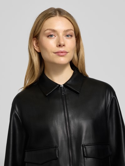 Modelka kobieca nosi czarną kurtkę w stylu skóry Jacke in Leder-Optik Modell 'Josmica' od OPUS, regularny krój, zamek, patki, zbliżenie górnej części ciała.