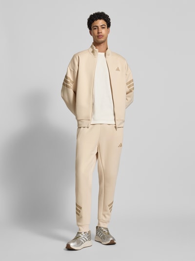Mannenmodel draagt Regular Fit Sweathose met Logoprint van adidas Sportswear, katoenmix, regular fit, elastische band met tunnelkoord, elastische boorden, binnenbeenlengte maat M 71 cm, beige tinten, gladde textuur, ganzkörperansicht van voren.