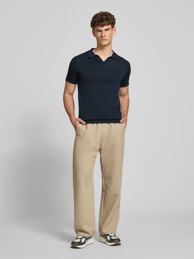 Männermodel trägt Regular Fit Poloshirt in Strick-Optik Modell 'Bray' von Blend, Reine Baumwolle, kurzärmelig, beige Hose, Ganzkörperansicht von vorne.