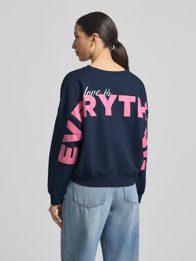 Frauenmodel trägt Regular Fit Sweatshirt aus reiner Baumwolle von Tom Tailor Denim in Dunkelblau mit pinkem Label-Schriftzug, unifarbene Optik, Rundhals, lange Ärmel, gerippte Abschlüsse, Sweat-Material, Ganzkörperansicht Rückansicht.