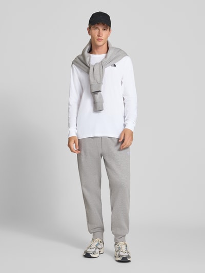 Męski model nosi bluzkę z długim rękawem z mieszanki bawełny Model 'EVOLUTION' od The North Face, luźny krój, wyhaftowane logo, elastyczne wykończenia, kolor biały, długość tyłu w rozmiarze M: 70 cm, widok całej sylwetki z przodu.