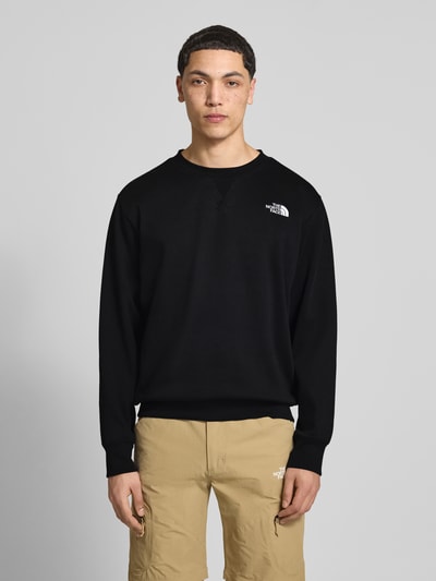 Męski model prezentuje Relaxed Fit Sweatshirt mit Label-Stitching Modell 'ESSENTIAL' von The North Face, czarny bawełniany miksem, z okrągłym dekoltem i elastycznymi wykończeniami, Ganzkörperansicht von vorne.