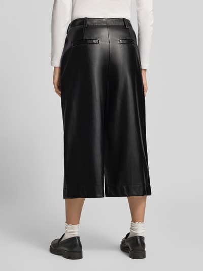 Frauenmodel trägt Straight Fit Hose in Midilänge mit Bundfalten von Oui in Leder-Optik, schwarze Farbe, Detail Bundfalten, Ganzkörperansicht Rückansicht.