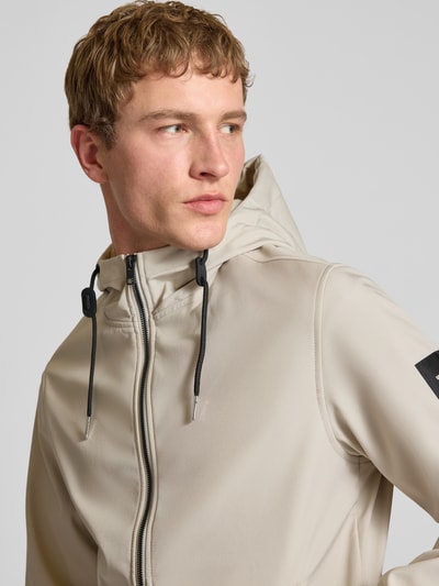 Männermodel trägt Softshelljacke mit Reißverschlusstaschen von Jack & Jones in Beige, Kapuze mit Tunnelzug, Nahaufnahme Oberkörper. 