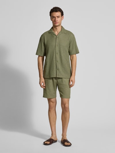 Männermodel trägt Regular Fit Freizeithemd mit Strukturmuster von MCNEAL in grün, Elastischer-Material-Mix, Kurzärmelig, Reverskragen, durchgehende Knopfleiste, Rückenlänge 72 cm, Schulterbreite 48 cm, Ärmellänge 25 cm, Ganzkörperansicht von vorne.