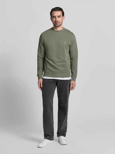 Męski model nosi Relaxed Fit Sweatshirt aus reiner Baumwolle Modell 'WESTART' od BOSS Orange, oliwkowy, jednolity, długi rękaw, naszywka z logo, dekolt okrągły, materiał bawełna, widok całej sylwetki z przodu.
