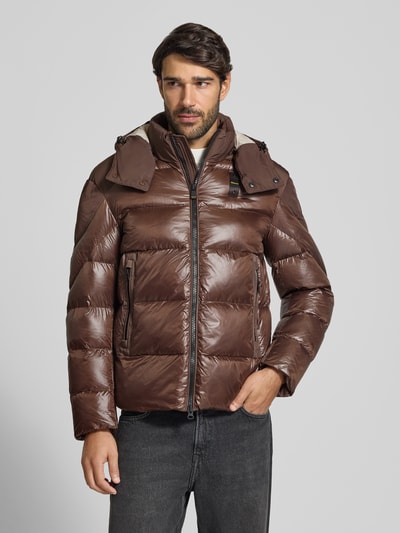 Męski model nosi Steppjacke mit Zweiwege-Reißverschluss Modell 'KIERNAN' von Blauer USA w kolorze brązowym, krój regular fit, z kapturem, detalem z logo, materiał o lekko błyszczącej teksturze; szerokość w rozmiarze M: 59 cm, długość tyłu: 67 cm, szerokość ramion: 49 cm, długość rękawa: 65 cm, widok całej sylwetki z przodu.