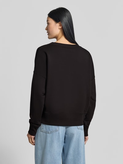 Frauenmodel trägt Relaxed Fit Sweatshirt aus reiner Baumwolle von miss goodlife, schwarzes Statement-Design mit Pailettenbesatz, Ganzkörperansicht Rückansicht.