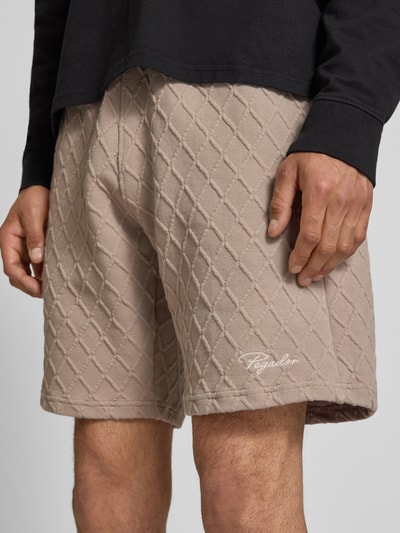 Männermodel trägt Relaxed Fit Shorts mit Strukturmuster Modell 'Jovren' von Pegador in Beige, Elastischer-Material-Mix, Nahaufnahme Oberschenkel, Bundweite 39 cm, Innenbeinlänge 24 cm bei Größe M.