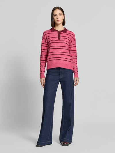 Frauenmodel trägt Strickpullover mit Woll-Anteil Modell 'SAGE' von ICHI in Rosa mit dunkelroten Streifen, relaxed Fit, Polokragen, gerippte Abschlüsse, kombiniert mit dunkelblauer Hose, Ganzkörperansicht von vorne.