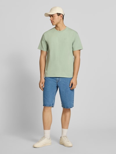 Männermodel trägt Loose Fit Jeansshorts aus reiner Baumwolle Modell '469' von Levi's® in Denim-Optik, 5-Pocket-Design, Label-Patch, Nieten, Kontrastnähte, Knopf und verdecktem Reißverschluss, Ganzkörperansicht von vorne.