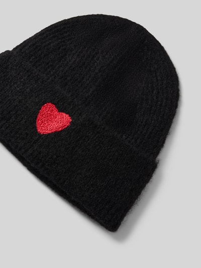 Produktfoto, schwarze Mütze mit Woll-Anteil von Jake*s Casual, rote Herzform als Akzent, strukturierte Oberfläche auf grauem Hintergrund.