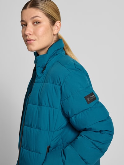 Frauenmodel trägt Jacke mit Daumenloch und Kapuze von NAUTGÅRD in Türkis, gesteppt, Zweiwege-Reißverschluss, Nahaufnahme Oberkörper.