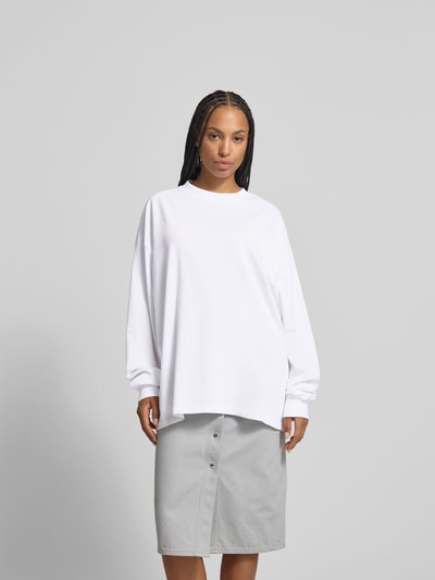 Frauenmodel trägt Oversized Longsleeve aus Baumwolle von black palms in Weiß, oversized mit Rundhalsausschnitt und elastischen Ärmelabschlüssen, Rückenlänge bei Größe S: 79 cm, Ganzkörperansicht von vorne.