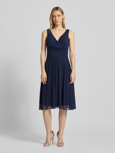 Frauenmodel trägt Cocktailkleid in Wickel-Optik mit V-Ausschnitt von TROYDEN COLLECTION, dunkelblau, Mesh, taillierter Schnitt, Midikleid, Drapierungen, Rückenlänge bei Größe 36: 108 cm, Brustweite bei Größe 36: 41 cm, Ganzkörperansicht von vorne.